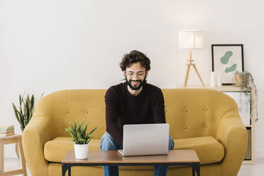 Lächelnder Mann mit Laptop auf dem Sofa im Wohnzimmer zu Hause - XLGF02919