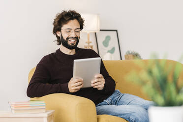 Glücklicher Mann bei einem Videogespräch über einen Tablet-PC im heimischen Wohnzimmer - XLGF02928