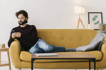 Man using mobile phone on sofa in living room at home - XLGF02934