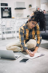 Junge Afro-Frau, die von zu Hause aus arbeitet und mit ihrem Laptop auf dem Boden sitzt - CAVF96477