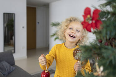 Cheerful blond girl with Christmas ornament at home - SVKF00129
