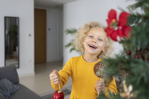 Fröhliches blondes Mädchen mit Weihnachtsschmuck zu Hause - SVKF00129