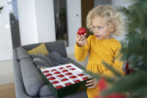 Blondes Mädchen betrachtet eine Kugel im heimischen Wohnzimmer - SVKF00132