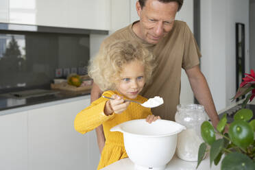 Lächelndes blondes Mädchen, das einen Löffel Mehl in der Hand hält, steht neben ihrem Vater in der Küche - SVKF00140