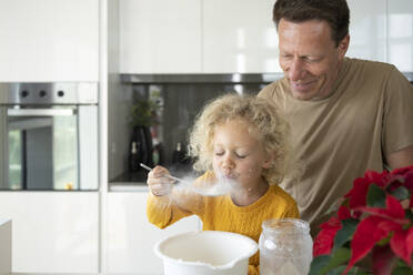 Lächelnder Mann sieht seine Tochter an, die in der Küche Mehl bläst - SVKF00142