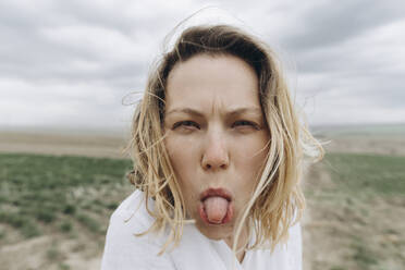 Verspielte Frau streckt ihre Zunge auf einem landwirtschaftlichen Feld heraus - SIF00075