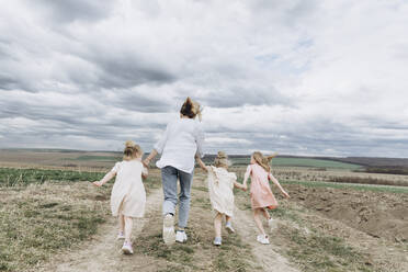 Frau mit drei Töchtern läuft auf einem landwirtschaftlichen Feld - SIF00081