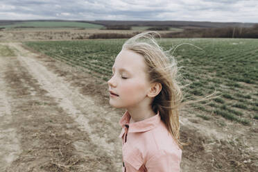 Mädchen mit geschlossenen Augen genießt den Wind in einem landwirtschaftlichen Feld - SIF00085