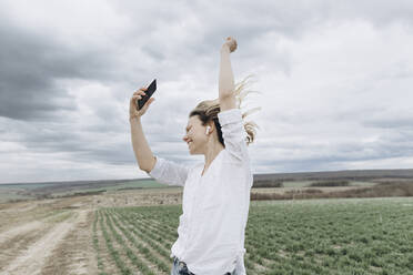 Frau tanzt und hört Musik über ihr Smartphone auf einem landwirtschaftlichen Feld - SIF00092