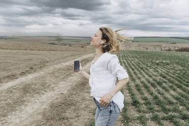 Lächelnde Frau hört Musik auf einem landwirtschaftlichen Feld - SIF00093