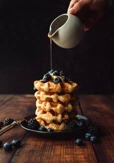 Maple syrup being poured over stack of belgian waffles with berries. - CAVF96491