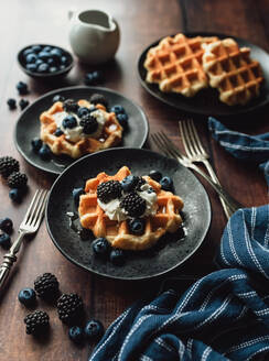 Teller mit belgischen Waffeln mit Beeren und Sahne auf einem Holztisch. - CAVF96492