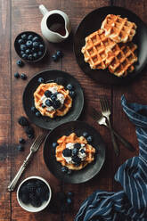 Draufsicht auf Teller mit belgischen Waffeln und Beeren auf einem Holztisch. - CAVF96493