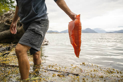 Ein Mann trägt ein frisches Lachsfilet aus dem Wasser - CAVF96522