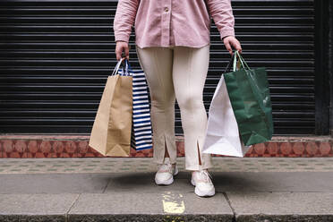 Woman with shopping bags standing on footpath - ASGF02269