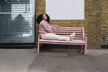 Young woman with eyes closed sitting on pink bench - ASGF02278