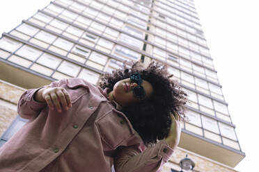 Junge Frau mit Sonnenbrille vor einem Gebäude stehend - ASGF02291