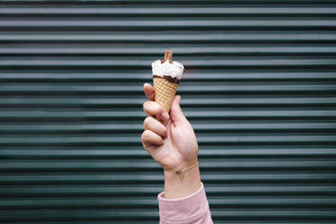 Hand of woman holding holding ice cream in front of shutter - ASGF02292