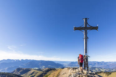 Deutschland, Bayern, Wanderin steht am Gipfelkreuz auf dem Geigelstein - FOF13130