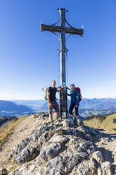 Deutschland, Bayern, Zwei Wanderer posieren vor dem Gipfelkreuz auf dem Geigelstein - FOF13131