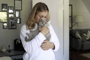Young woman kissing gray cat at home - FLLF00645