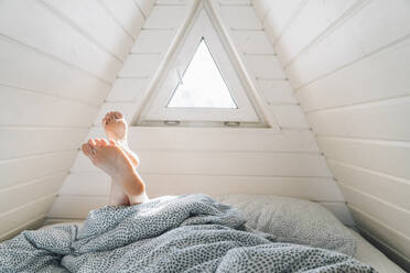 Sonnenlicht fällt durch das Fenster auf die Beine einer Frau, die auf einem Bett im Dachgeschoss liegt - VPIF05923