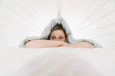 Verängstigte Frau liegt unter einer Decke auf dem Bett im Dachgeschoss - VPIF05928