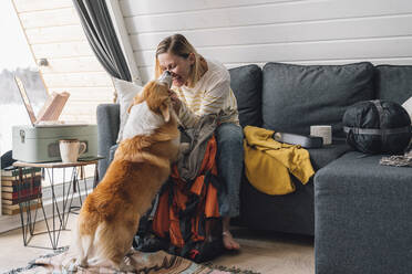 Lächelnde Frau streichelt Hund, der zu Hause auf dem Sofa sitzt - VPIF05930