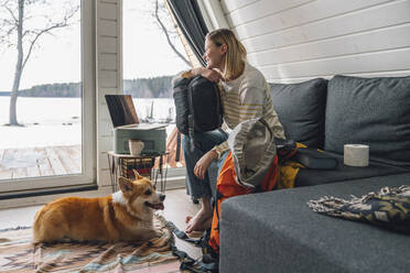 Frau mit Rucksack auf Sofa sitzend bei Hund zu Hause - VPIF05931