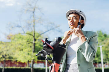 Geschäftsfrau mit Fahrradhelm auf einem Elektroroller - MEUF05227