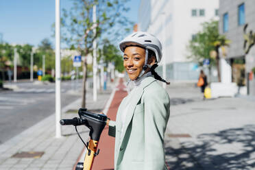 Lächelnde Frau mit Elektro-Scooter an einem sonnigen Tag - MEUF05229