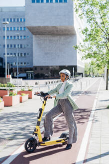 Young businesswoman with electric push scooter by office building - MEUF05233