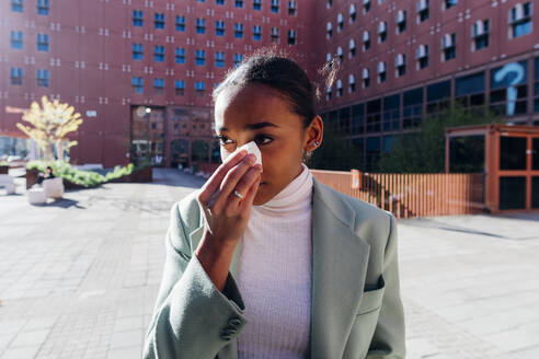 Traurige Geschäftsfrau wischt sich vor einem Bürogebäude die Tränen mit einem Taschentuch ab - MEUF05245