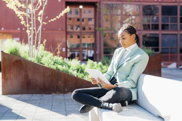 Young businesswoman freelancing over tablet PC sitting on bench - MEUF05249