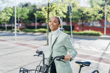 Nachdenkliche Geschäftsfrau mit Elektrofahrrad auf dem Fußweg - MEUF05261