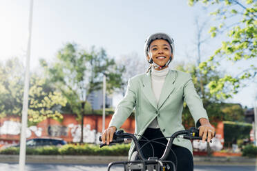 Junge Geschäftsfrau mit Helm auf einem Elektrofahrrad auf der Straße - MEUF05268
