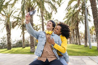 Happy man taking selfie with girlfriend through smart phone at public park - OIPF01650