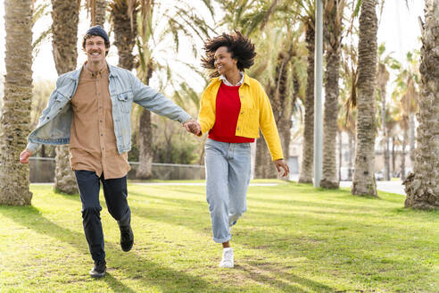 Cheerful couple running together at park - OIPF01664