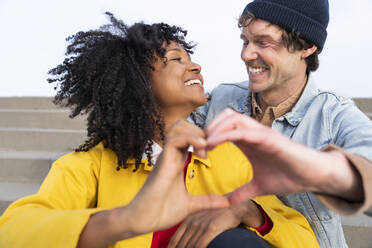 Cheerful couple gesturing heart shape looking at each other - OIPF01670