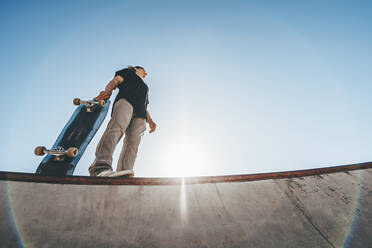 Mann mit Skateboard im Skateboardpark an einem sonnigen Tag - OMIF00769