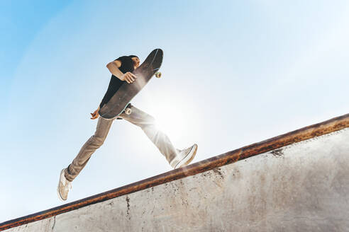 Mann mit Skateboard im Skateboardpark an einem sonnigen Tag - OMIF00770