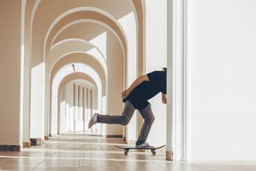 Man with skateboard practicing in arcade - OMIF00774