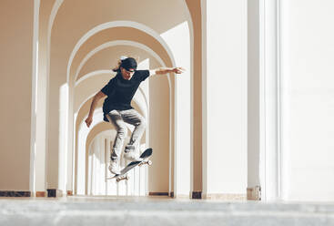 Man practicing jump with skateboard in arcade - OMIF00776