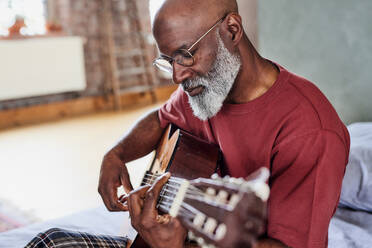 Man with eyeglasses playing guitar at home - FMKF07457