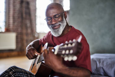 Smiling mature man playing guitar at home - FMKF07459