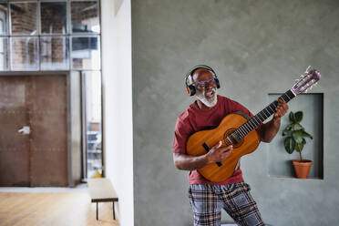 Mann mit Kopfhörern spielt Gitarre und singt zu Hause - FMKF07462