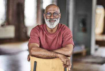 Bald man with eyeglasses on chair at home - FMKF07476