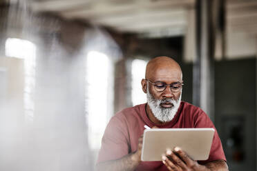 Man with beard using tablet PC at home - FMKF07477