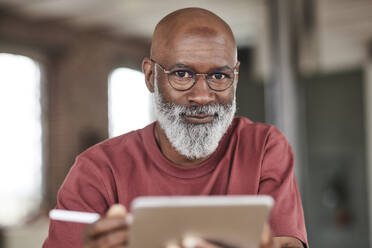 Mature man with beard holding tablet PC at home - FMKF07482