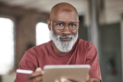 Älterer Mann mit Bart hält Tablet-PC zu Hause - FMKF07482